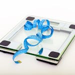 A digital glass weighing scale with a blue measuring tape, symbolizing weight management.