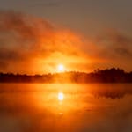 Calm sunrise over a misty lake with vibrant orange hues in the sky.