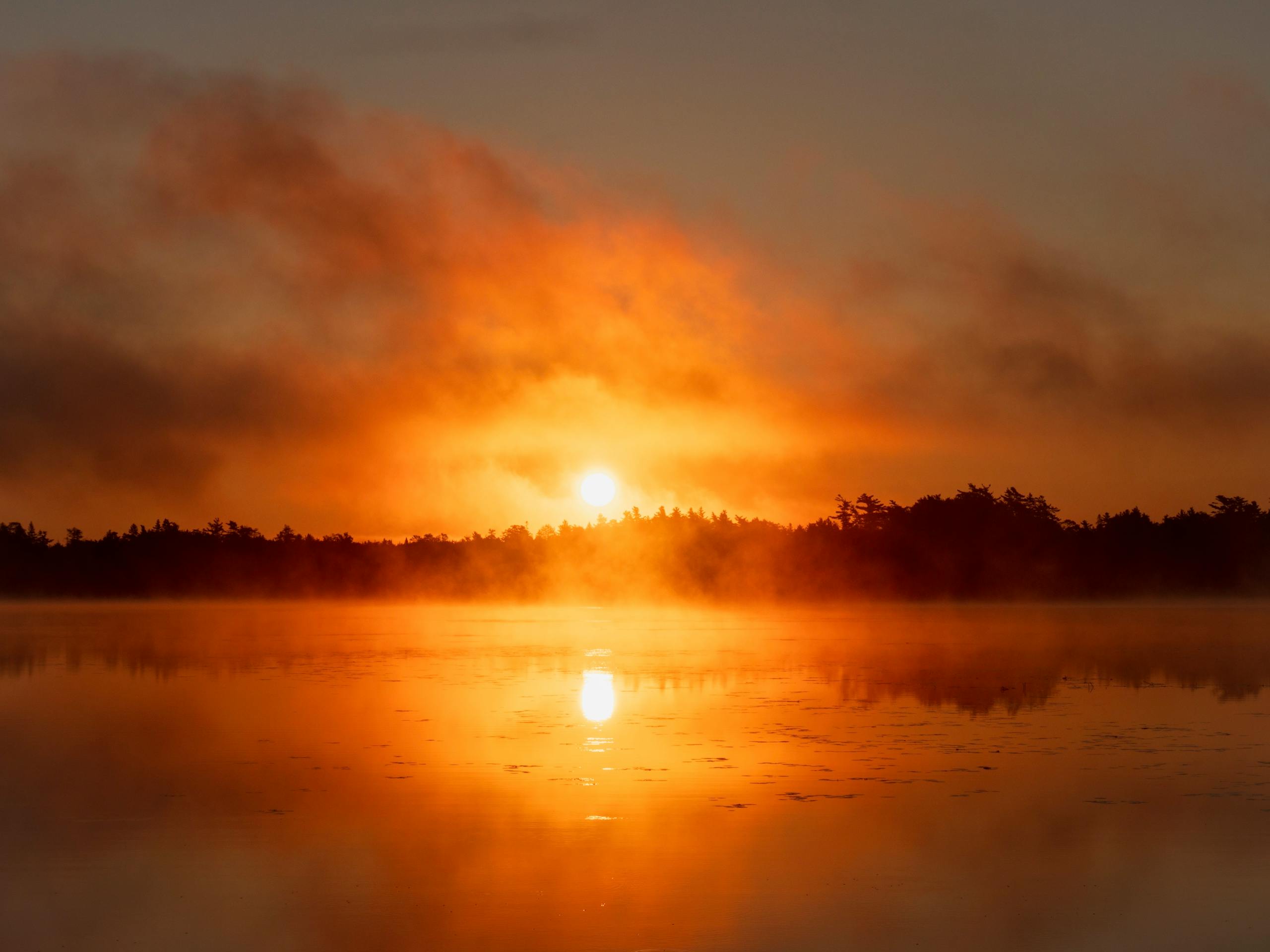 Calm sunrise over a misty lake with vibrant orange hues in the sky.