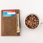 Top view of a leather wallet with credit cards and a cup filled with coffee beans on a white background.