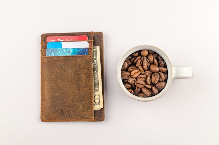 Top view of a leather wallet with credit cards and a cup filled with coffee beans on a white background.